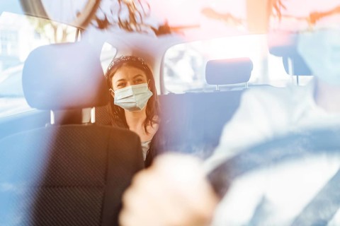 A woman wearing a protective mask sitting on the back seat of a taxi car