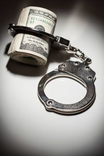 Handcuffs locked on roll of one hundred dollar bills under spotlight