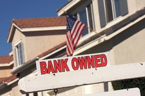 Bank owned real estate sign and house with american flag in the background