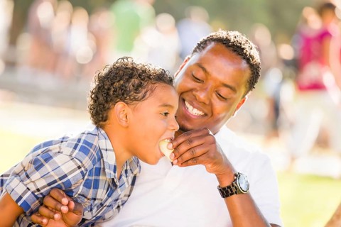 African american father and mixed-race son eating an apple in the park