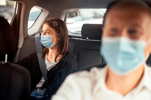 A woman wearing a protective mask sitting on the back seat of a taxi car