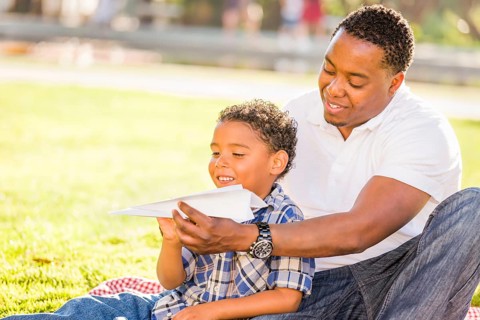 Happy african american father and mixed-race son playing with paper airplanes in the park