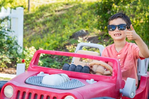Young mixed-race chinese and caucasian boy wearing sunglasses playing in toy car