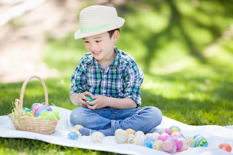 mixed-race chinese and caucasian boy outside wearing rabbit ears playing with easter eggs