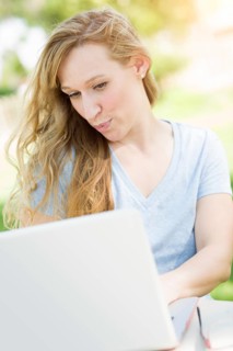 Young adult woman live video chatting outdoors using her laptop