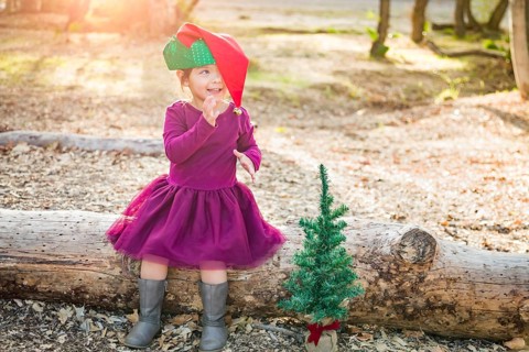 Cute mixed-race young baby girl having fun with christmas hat and tree outdoors