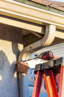 Worker attaching aluminum rain gutter and down spout to fascia of house