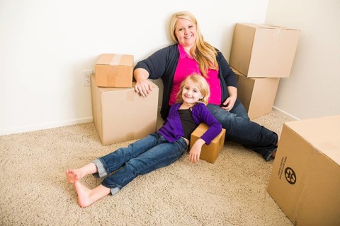 Happy young mother and daughter in empty room with moving boxes