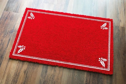 Blank holiday red welcome mat with holly corners on wood floor background