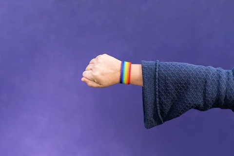 Detail of arm and hand of woman wearing gay wristband on purple background