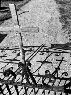Wrought iron gate with metal cross casting shadows on a path