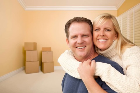 Happy affectionate couple in room of new house with only boxes on the floor