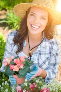Happy young adult woman wearing hat and gloves gardening outdoors