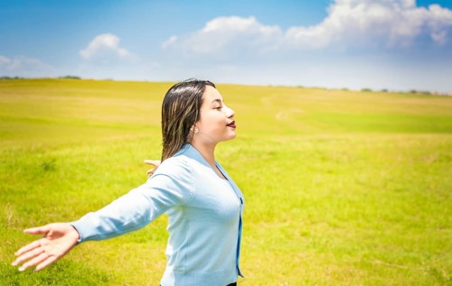 Happy woman breathing fresh air in the field and spreading arms