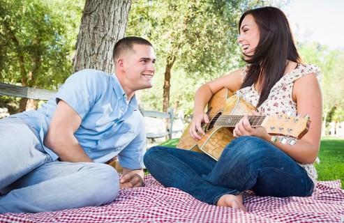 Young adult girl playing guitar with boyfriend in the park