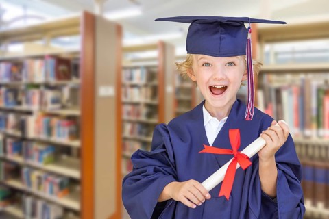 Cute young caucasian boy wearing graduation cap and gown in the library