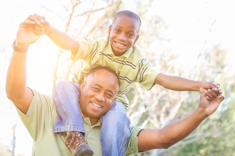 Happy african american father and son riding piggyback outdoors at the park