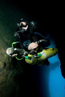 Diver dives into entrance of underwater cave with special equipment Diving equipment for cave divers