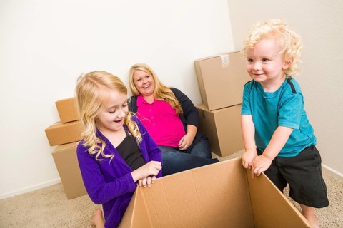 Playful young family in empty room playing with moving boxes