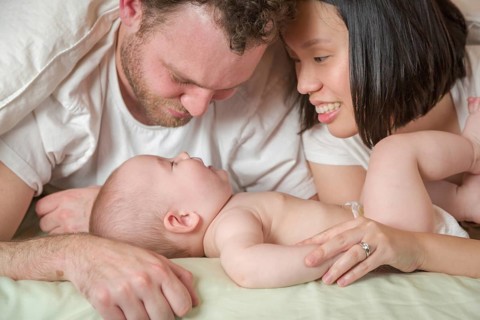 mixed-race chinese and caucasian baby boy laying in bed with his father and mother