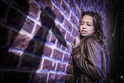 Male shadow figure with knife threatens frightened young woman against brick wall