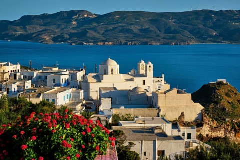 Picturesque scenic view of Greek town Plaka on Milos island over red geranium flowers and Orthodox greek church