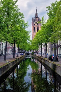Delt canal with old houses bicycles and cars parked along and Oude Kerk Old church tower. Delft