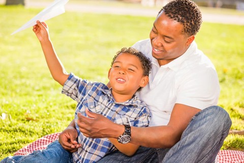 Happy african american father and mixed-race son playing with paper airplanes in the park