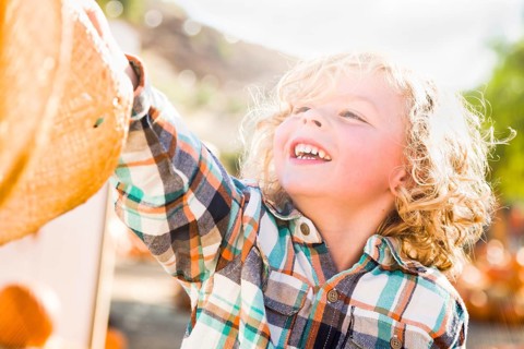 Little boy sitting with A cowboy hat in a rustic ranch setting at the pumpkin patch