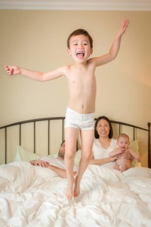Young mixed-race chinese and caucasian boy jumping in bed with his family