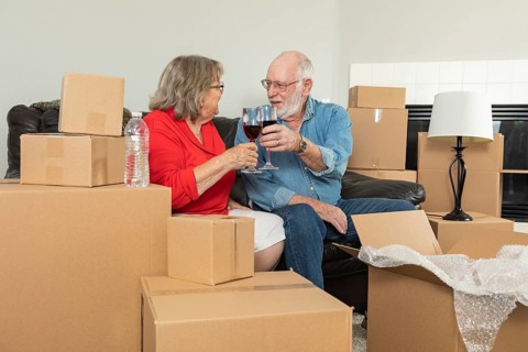 Senior adult couple toasting wine glasses surrounded by moving boxes