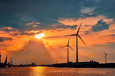 Wind turbines power electricity generators in Antwerp port on sunset