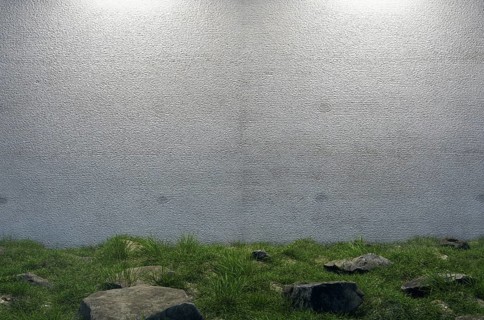Mysterious blank cement wall surrounded by large rocks and grass in field