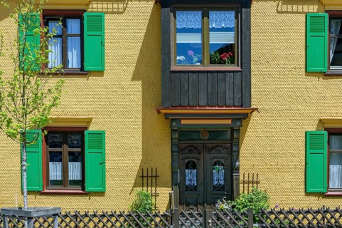 Yellow wooden shingle facade with bay window and green shutters