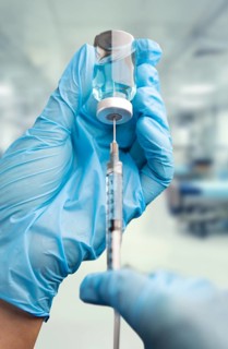Doctor or nurse wearing surgical gloves holding vaccine vial and medical syringe within hospital
