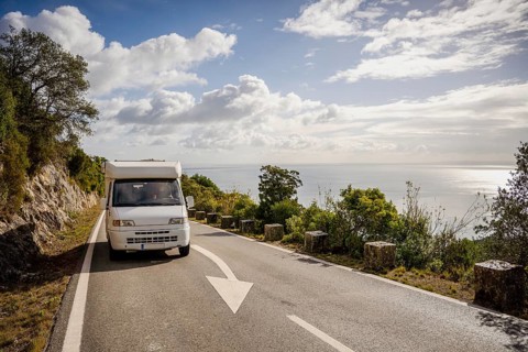 Small camper van driving on scenic road with sea views in Arrabida Natural Park