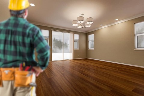 Contractor in hard hat and construction belt facing newly remodeled house room