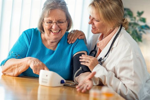 Senior adult woman learning from female doctor to use blood pressure machine