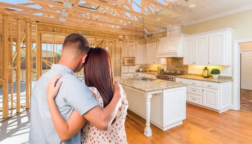 Young military couple facing house construction framing gradating into finished kitchen build