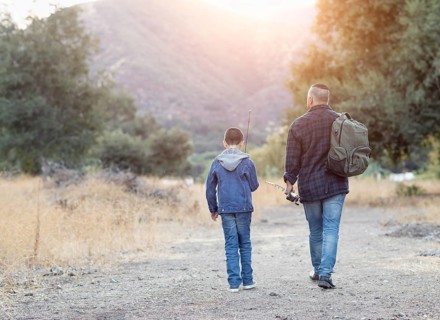 mixed-race father and son outdoors walking with fishing poles
