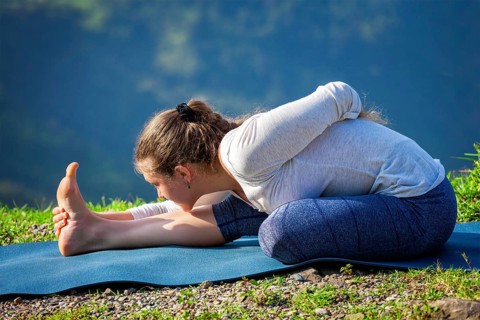 Woman doing Ashtanga Vinyasa yoga asana Ardha baddha padma paschimottanasana half bound lotus intense west stretch poser outdoors in mountains in the morning in Himalayas