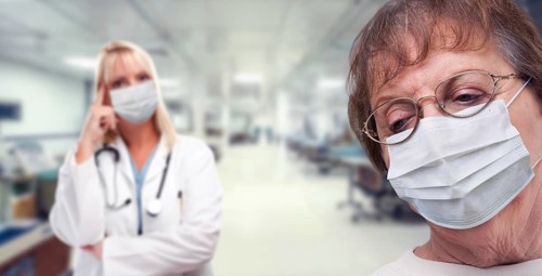 Senior adult female looking down as doctor stands behind all wearing medical face masks within hospital