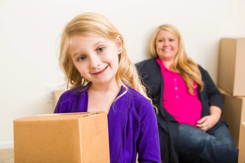 Happy young mother and daughter in empty room with moving boxes