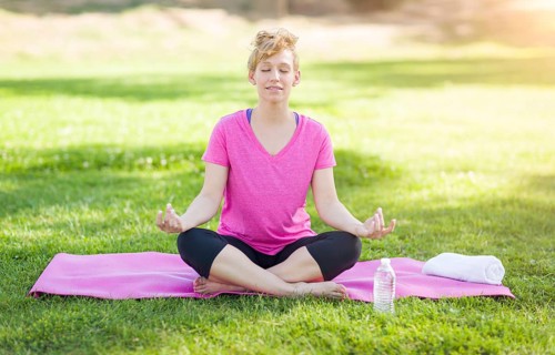 Young fit adult woman outdoors on the grass doing yoga