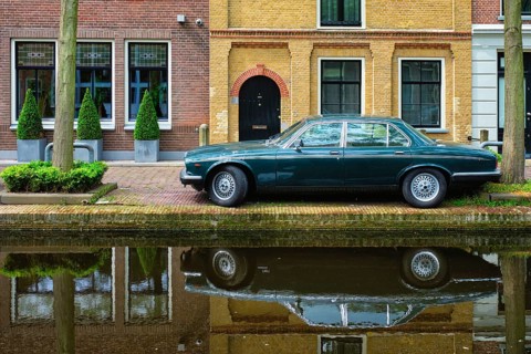 Old black retro car on canal embankment in street of Delft with reflection. Delft