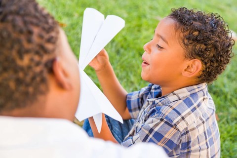 Happy african american father and mixed-race son playing with paper airplanes in the park