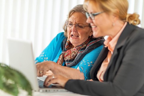 Woman helping senior adult lady on laptop computer