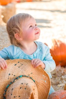 Adorable baby girl with cowboy hat in a country rustic setting at the pumpkin patch