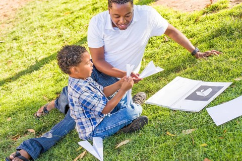 Happy african american father and mixed-race son playing with paper airplanes in the park