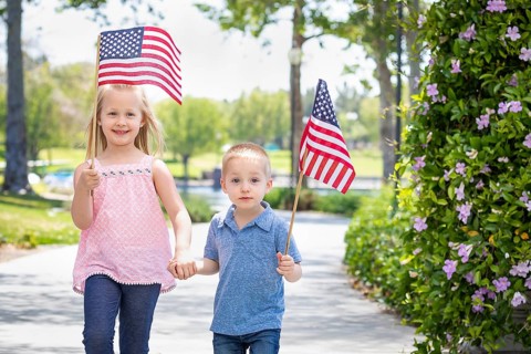Young sister and brother waving american flags at the park